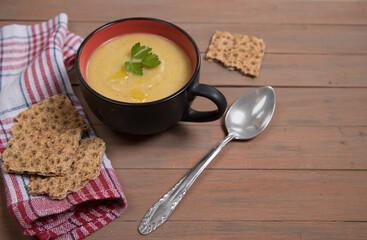 A plate of pumpkin soup on a brown wooden background , cereal loaves on a red napkin. Place for a copy space