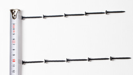 Black self-tapping screw and measuring roulette on a white background banner with space for text. Construction tools, fastening hardware.