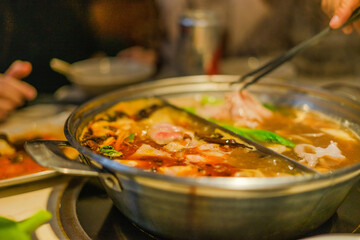 Hand using chopsticks pick raw sliced beef, vegetable, a piece of corn over the Chinese spicy hot pot, Szechuan Spicy Hot Pot