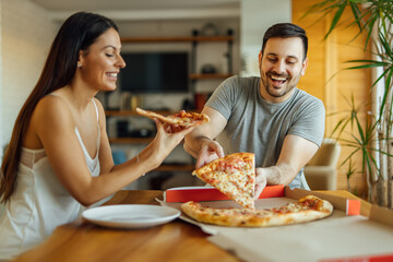 Cheerful couple in pajamas eating pizza at home, portrait.