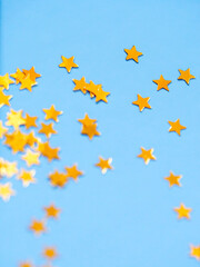 Gold star glitter confetti splashed on blue paper background.