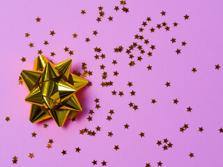 Gold bow with star glitter confetti on pink paper background.