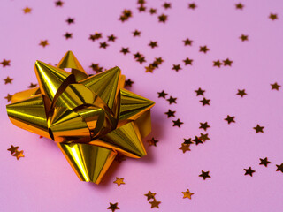 Gold bow with star glitter confetti on pink paper background.