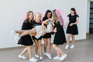 Fototapeta premium Beautiful sexy young girls in dress and veil on bachelor party. Bride hugging bridesmaids smiling outdoors and celebrating bachelorette party. Maiden evening, Hen-parties. Place for text.