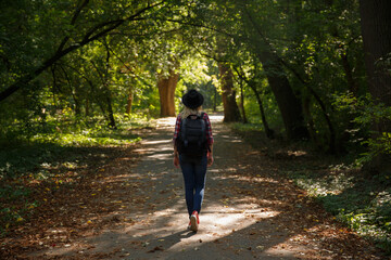 young caucasian girl travels in a hat and with a backpack through the forest or park in the shade of trees .background blurred. 