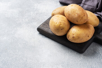 Several tubers of raw potatoes on a grey concrete background. Copy space.