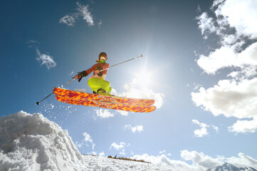 woman skier athlete makes a jump in flight on a snowy slope against the backdrop of a blue sky of mountains and clouds. Freeride and extreme skiing for women