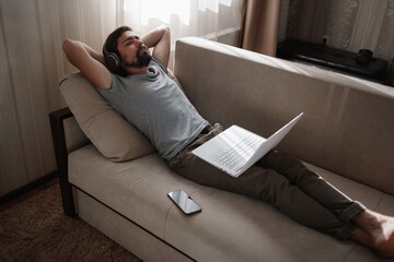 Man on sofa with headphones and notebook at home