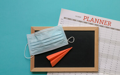 Face mask on top of blackboard and calendar planner with paper plane