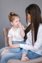 Portrait of attractive young woman with cute daughter. Mom and daughter sits on sofa in studio