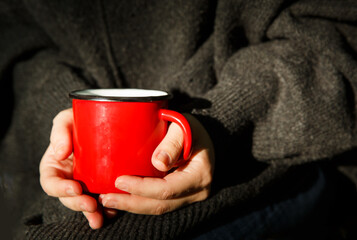 red metal mug in the hands of a girl in a gray sweater.selective focus. High quality photo