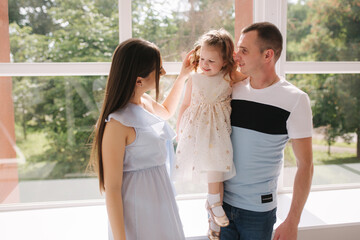 Family portrait of mom dand and little daughter in front of big window. Happy family