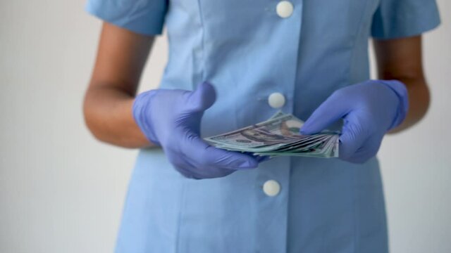 female hands of a doctor in special clothes take a pack of 100 money and hide it in her pocket