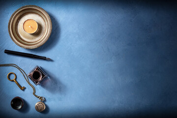 Vintage background with copy space, with an old watch, a key, ink well and pen, and a candle, a flat lay on a blue background