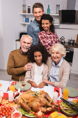 Selective focus of multicultural family hugging near turkey on table during thanksgiving