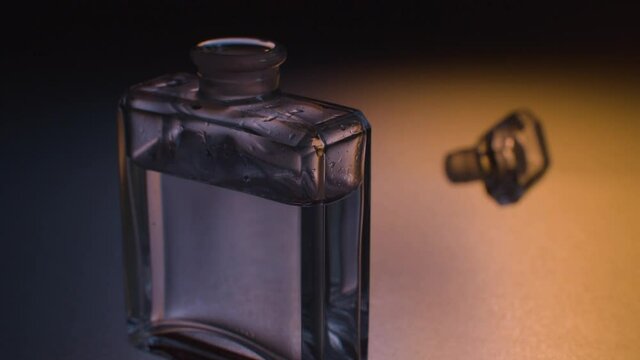 Close up glass bottle of perfume and lid on a glass table.