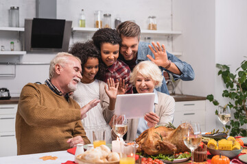Selective focus of multicultural family waving at digital tablet during video call and thanksgiving celebration