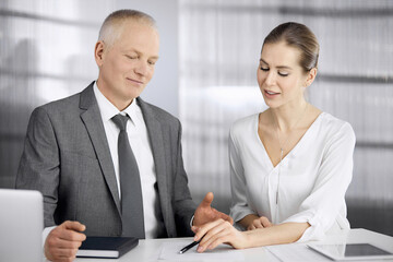 Elderly businessman and woman sitting and communicating in office. Adult business people or lawyers working together as a partners and colleagues at meeting. Teamwork and cooperation concept