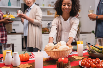 Selective focus of african american kid holding basket with buns near parents during thanksgiving dinner