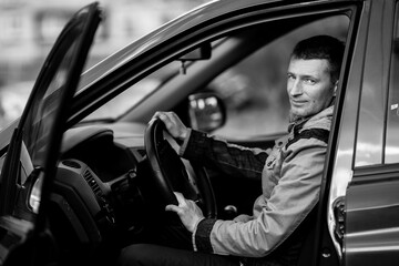 Man sits behind the wheel of a car. Black and white photography.