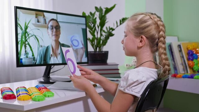 children remote education, schoolgirl shows cards with numbers during math lesson for her teacher in computer screen at home