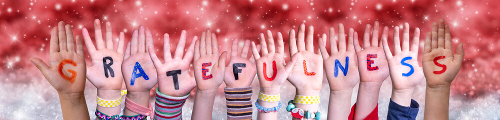 Children Hands Building Colorful English Word Gratefulness. Red Snowy Christmas Winter Background With Snowflakes And Sparkling Lights