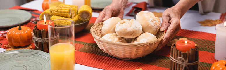 Panoramic shot of elderly woman holding basket with buns near thanksgiving dinner