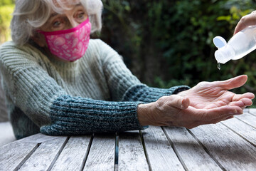 Woman Giving Hand Sanitizer To Senior Female Wearing Mask At Socially Distanced Meeting