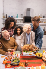 Selective focus of multiethnic family holding tasty turkey near candles on table