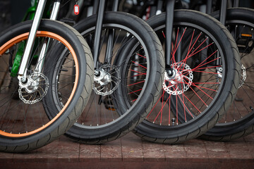 A close-up of the front wheels of a bicycle with disc brakes. Vintage city bicycles parked at a store or rental.