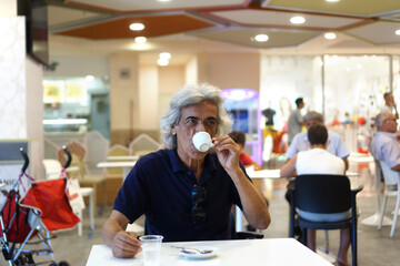 a mature man with long white hair takes a coffee smiling