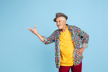 Cheerful sending kisses. Portrait of senior hipster man in stylish hat isolated on blue studio...