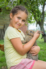 In the summer afternoon, a girl sits in the garden and holds a rabbit in her arms.