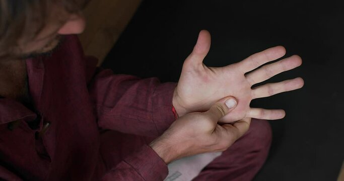 Top view of faceless man massaging palm indoors close up natural light slow motion. Unrecognizable white masseur stretching pressing hand detailed macro shot. Health energy body care concept