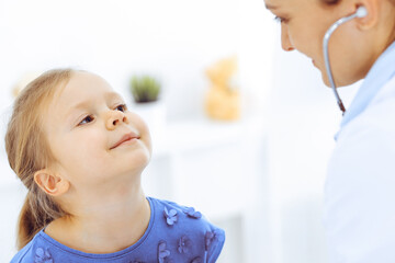 Doctor examining a little girl by stethoscope. Happy smiling child patient at usual medical inspection. Medicine and healthcare concepts