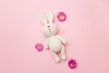 Knitted rabbit amigurumi with flowers chrysanthemums isolated on a pink background. Baby background. Copy space, top view