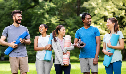 fitness, sport and healthy lifestyle concept - group of happy people with yoga mats at park