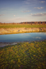 A small drying pond in the evening in the field. Cloudy sky over the lake. Landscape.