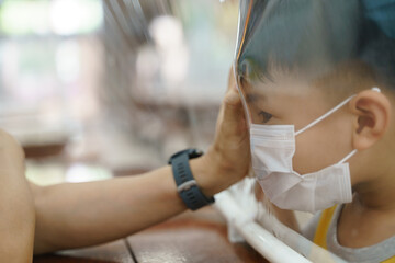 Asian mother and son wearing masks and keep touching each other through plastic sheet