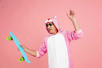 Skater in cool eyewear. Portrait of senior hipster man in stylish attire isolated on pink studio background. Tech and joyful elderly lifestyle concept. Trendy colors, forever youth. Copyspace © master1305