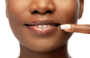 Naklejka premium beauty, dental care and people concept - close up of face of beautiful smiling young african american woman pointing to her mouth over white background