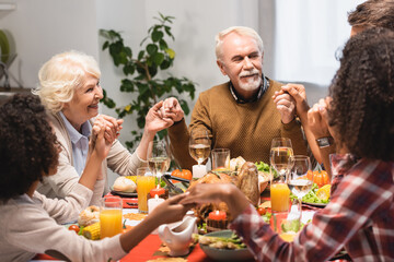 Multiethnic family holding hands near dinner on thanksgiving holiday