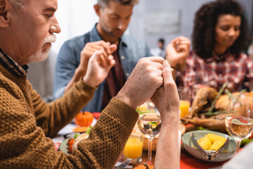 selective focus of senior man holding hands with multicultural family on thanksgiving