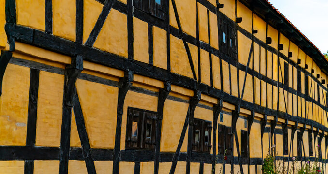 Facade of an old half timbered medieval house in northern Europe, with black wood window shutters and yellow chalk wall.