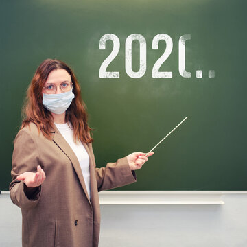 Teacher in face mask at the blackboard with the year the quarantine ends in the future. School quarantine education concept