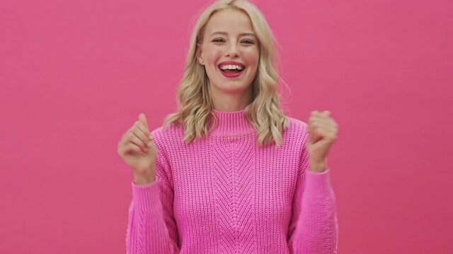 A smiling blonde woman in a pink sweater is nodding standing isolated over a pink background