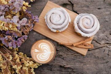Top view Cinnamon Rolls in a wooden plate and coffee latte on a wooden table and flower background 