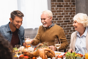 joyful senior man holding bun while celebrating thanksgiving day with family