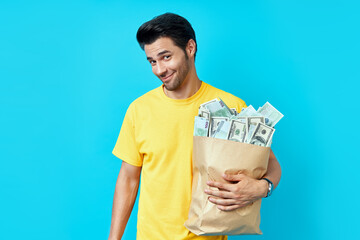 Funny man hold paper bag full of stacks of money isolated on blue background