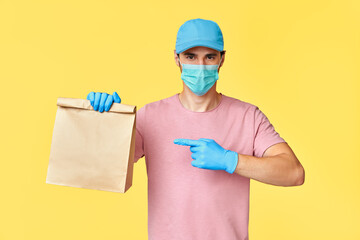 Fototapeta na wymiar Delivery man pointing on paper packet with food wearing face mask and gloves